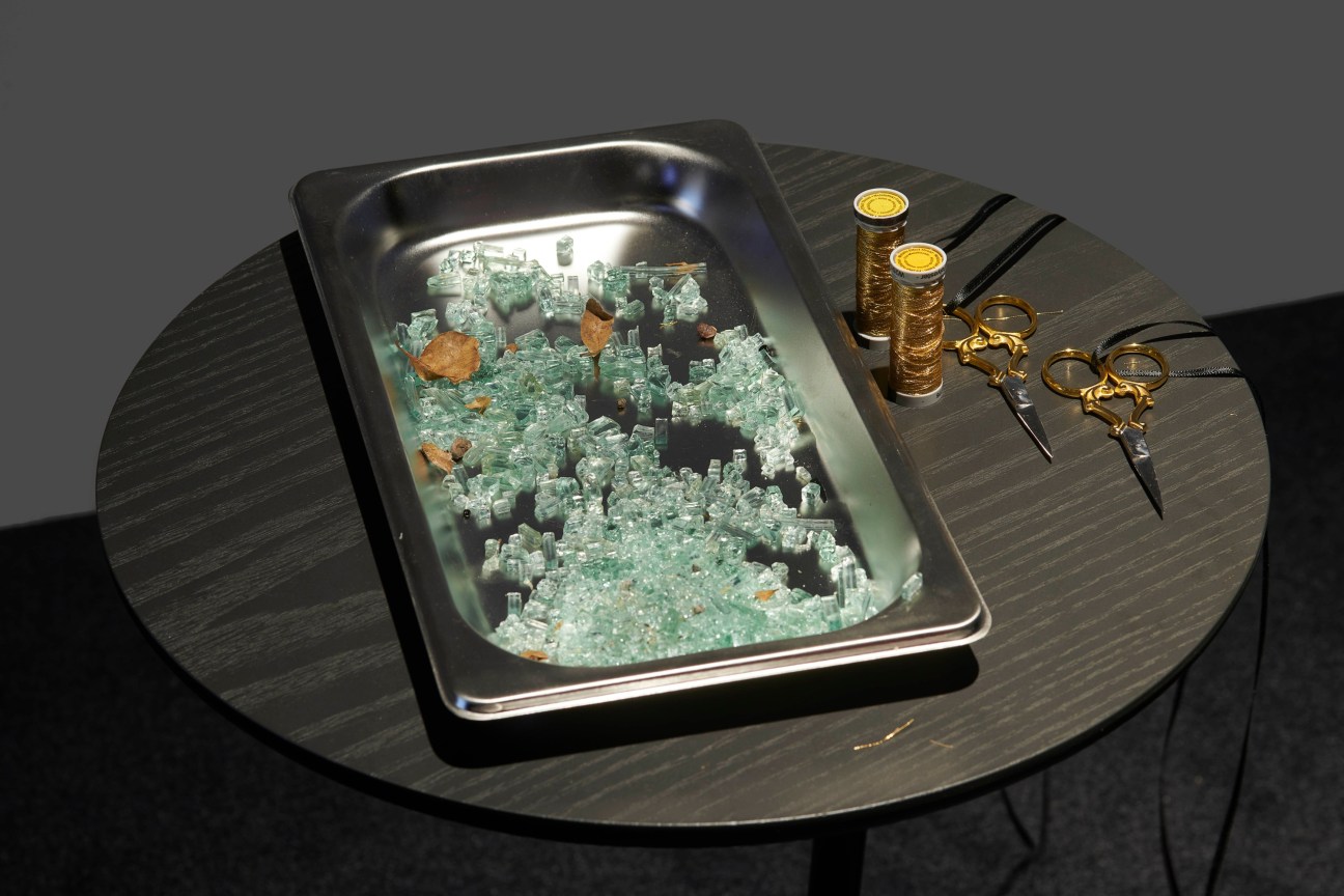 a table holding a tray with broken glass next to gold wire and scissors