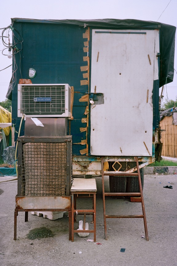 aqua wooden shack with a white door and a silver lock with a set of rusty stairs leading up to it, old AC machines are to the left of the door
