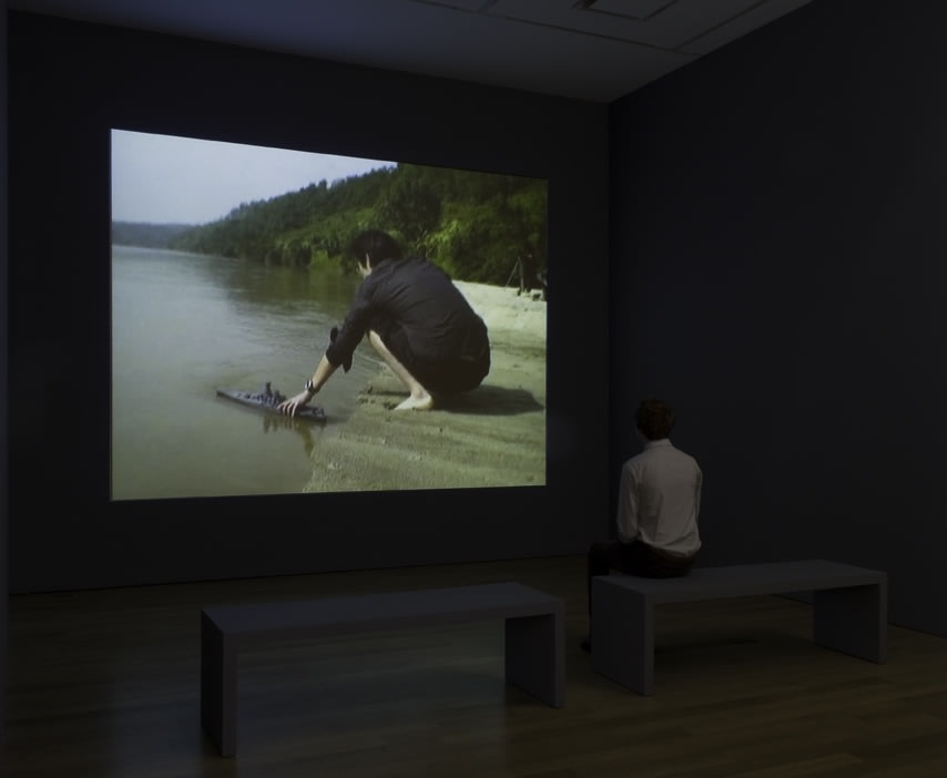 film of a man plcing a toy boat in a big body of water