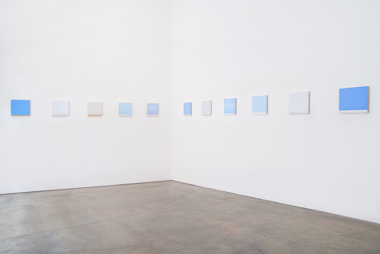Installation view of several square canvases in a row spanning two walls