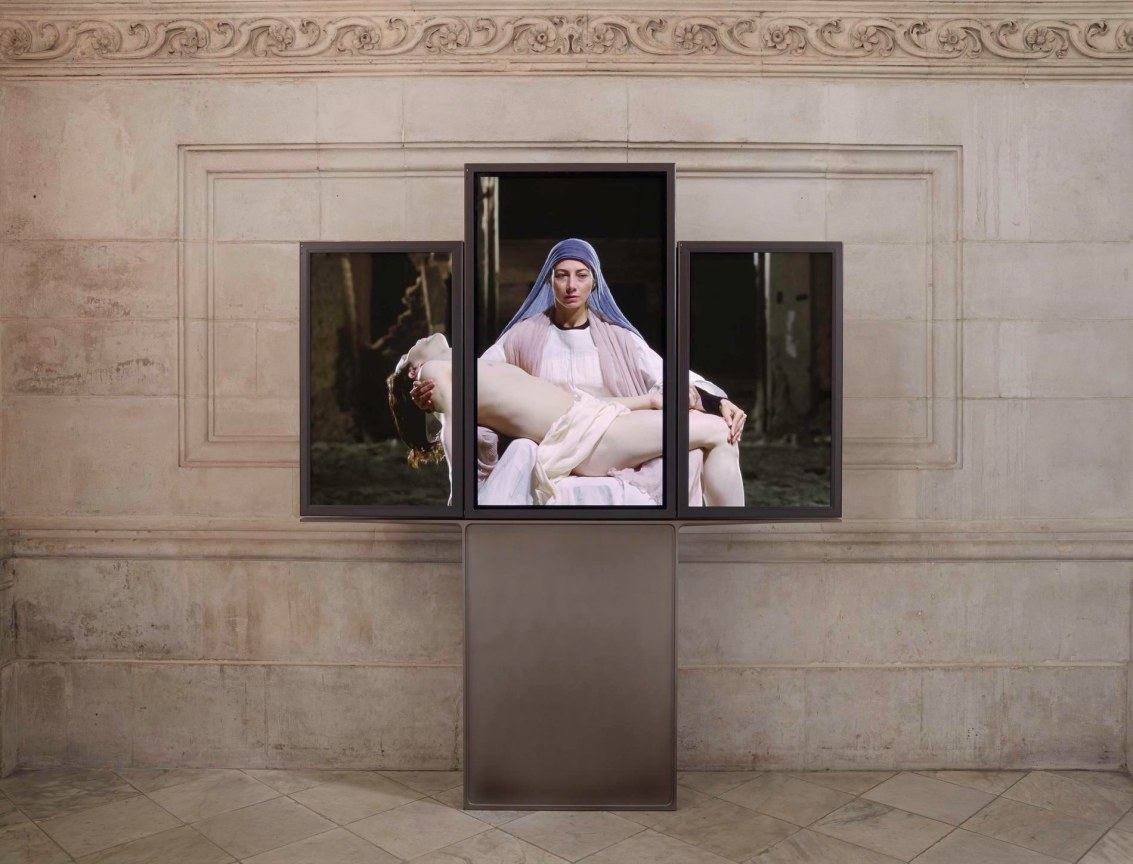 woman dressed as the Virgin Mary holds and adult Jesus on her lap