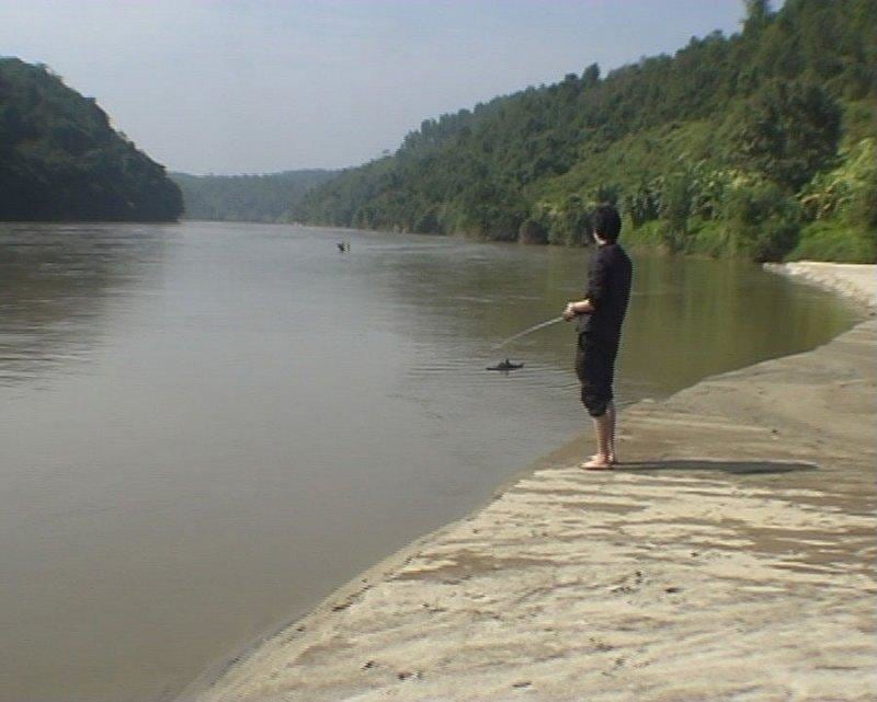man standing near a river controlling a tiny boat