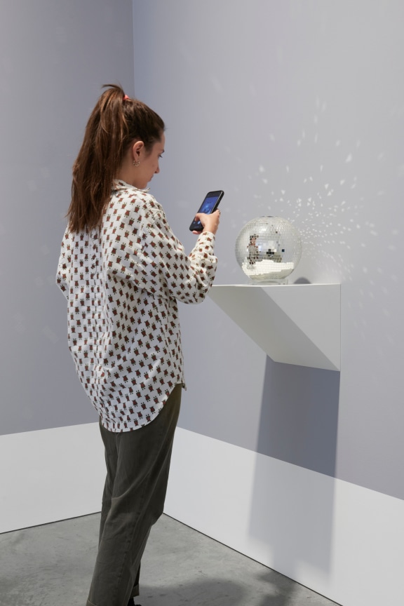person taking a picture of a small mirror ball with their smart phone
