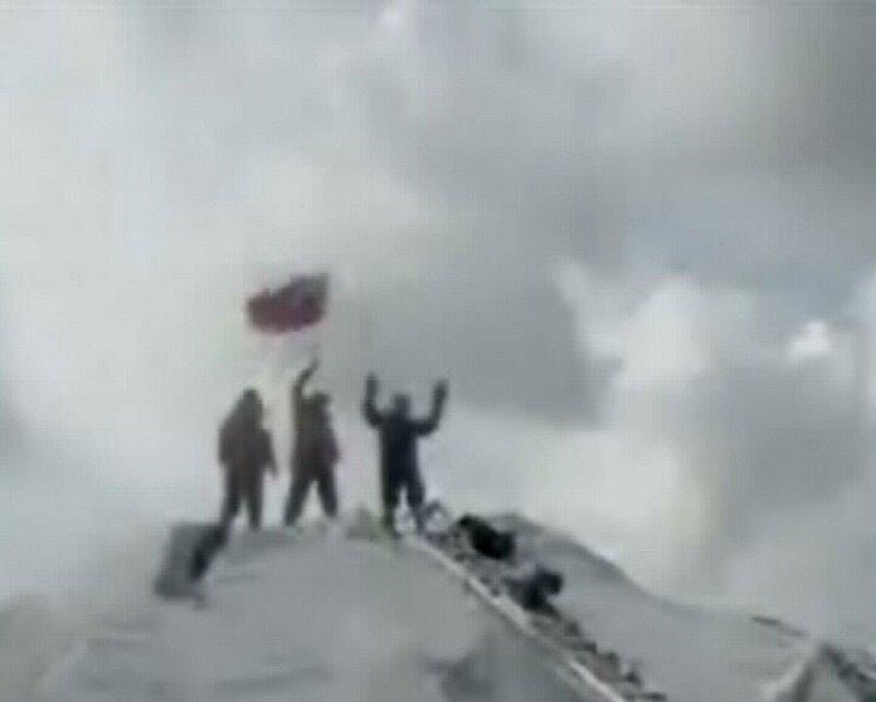 three men standing a top a hill-like figure