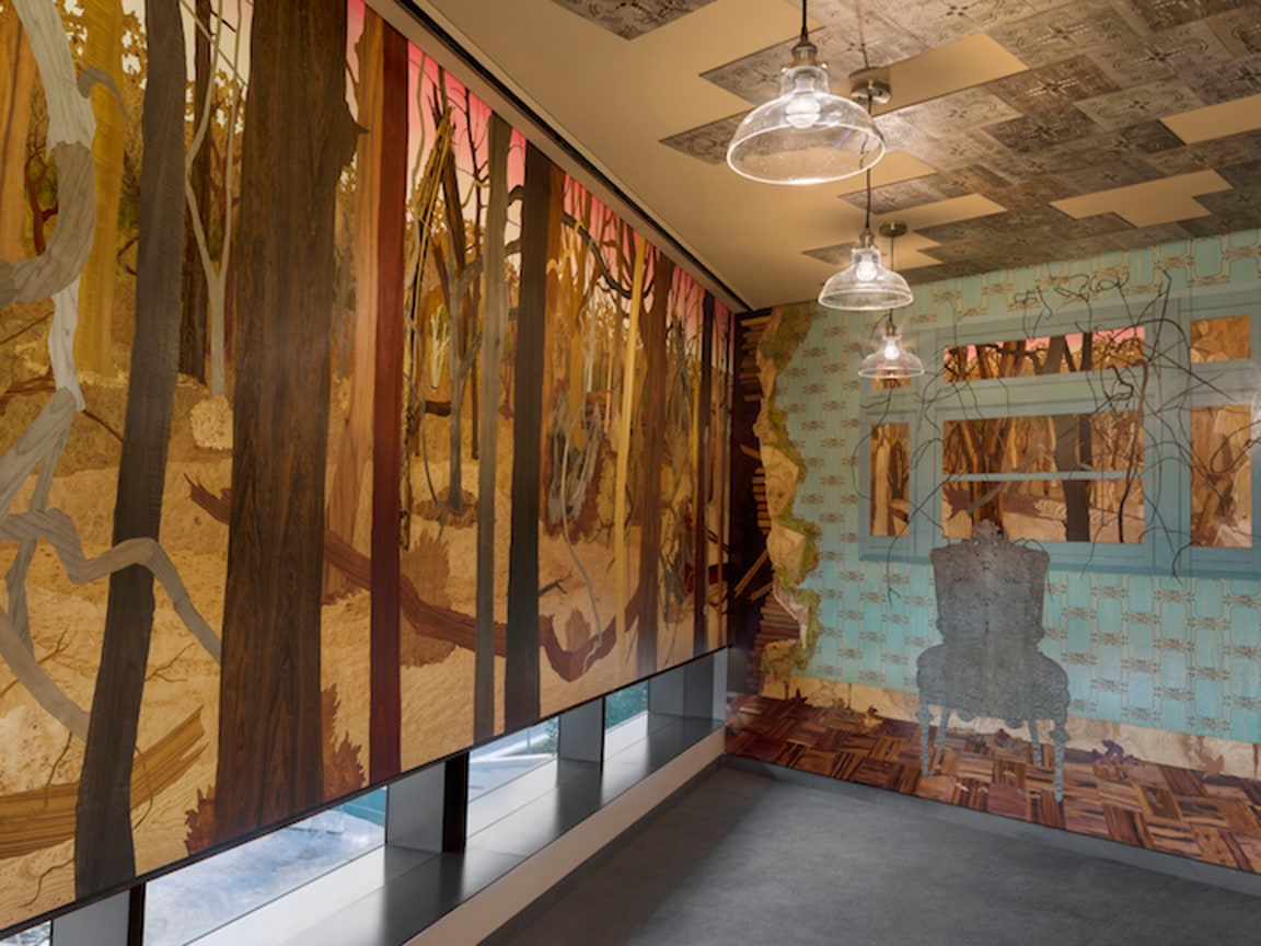 two walls covered in wooden veneer, one is a landscape of a dead forest while the other is an abandoned home interior