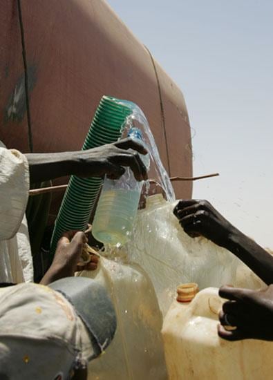 water comming out of a green tube while several hands holding empty jugs surround it