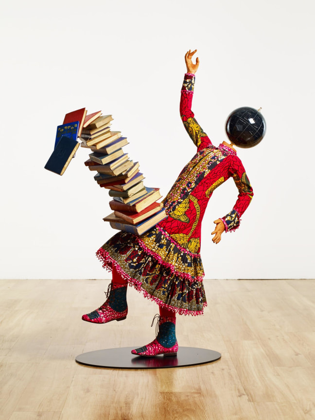 mannequin with a globe for a head balancing a stack of books on her knee