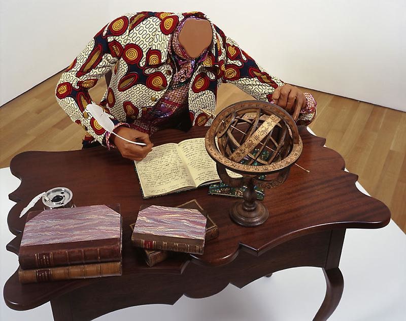headless mannequin sitting at a desk and writing