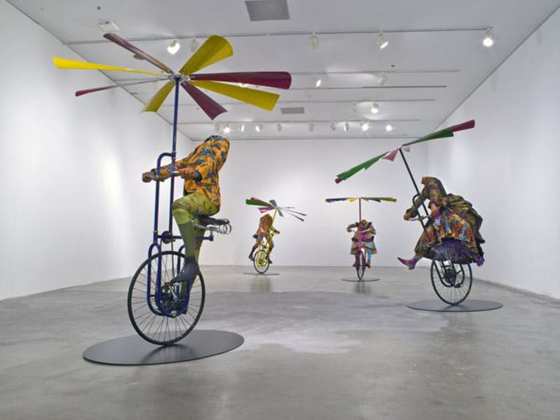 installation view of headless mannequins riding flying machines