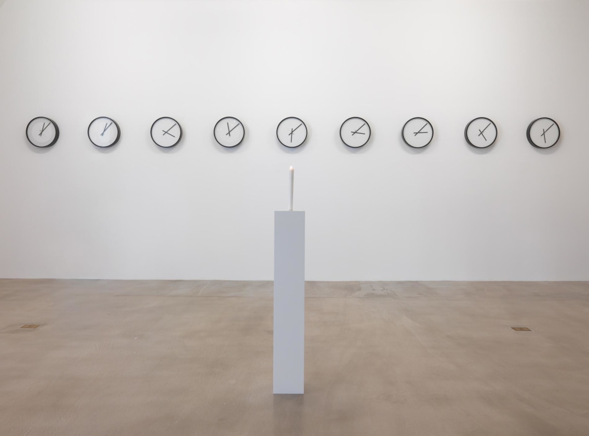 installation view of a candle and several clocks set to different times