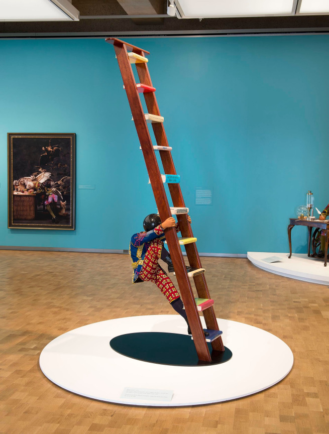 mannequin with a globe for a head climbing a ladder from the wrong side; the ladder has books for steps