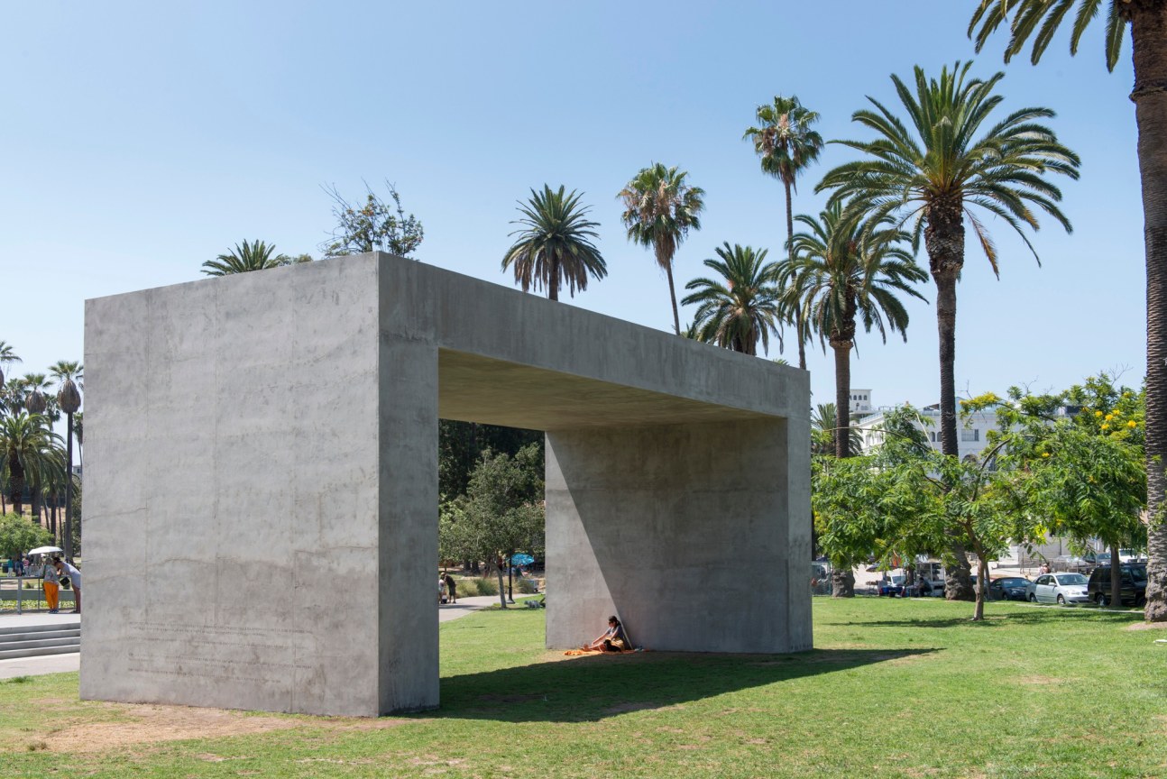 giant concrete structre made of cement placed in what looks like a park; a person is seen sitting under it