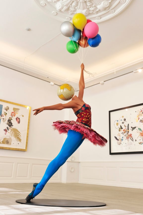 a mannequin with a globe for a head dancing ballet and holding different colored balloons
