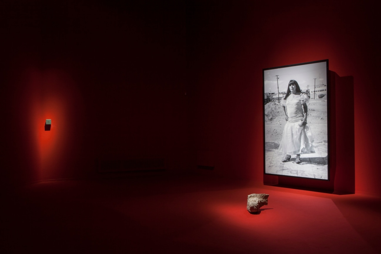 Installation view of photograph of a sex worker standing in deserted area and a rock placed on floor in front of the photo