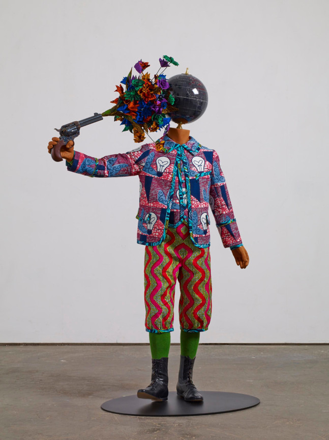 mannequin with a globe for a head holding a gun and shooting himself at the head with flowers