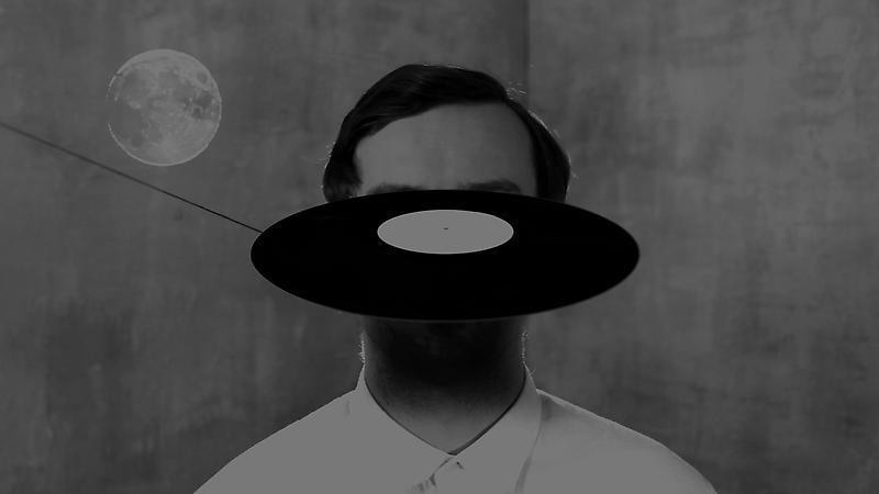 a record floats in front of a man's face; a silhouette of the moon is seen on the top left corner of the image