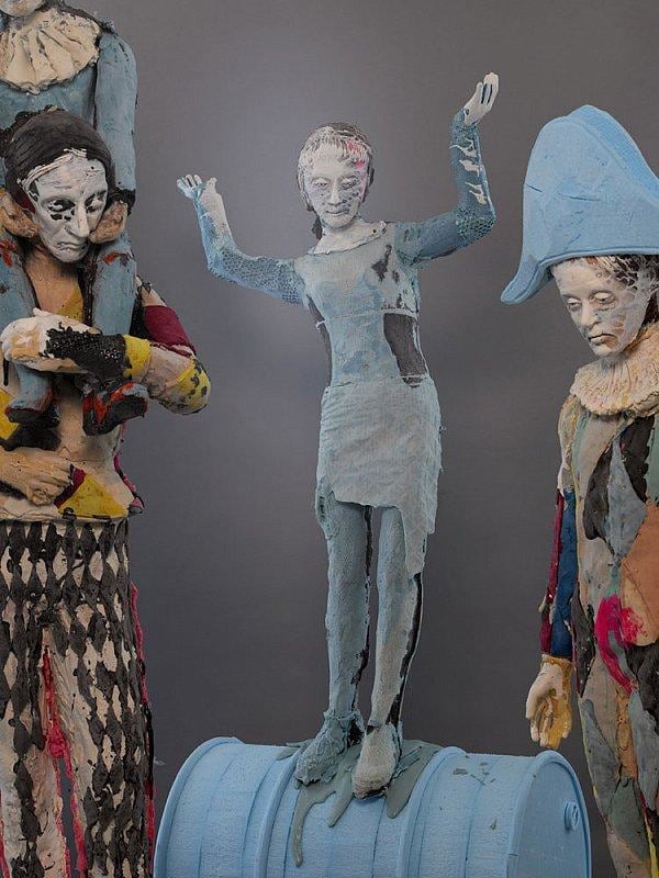 statue of a child standing on a metal barrel by other statues with forlorn expressions