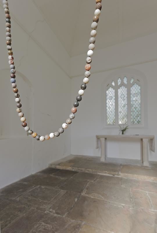 close up of a necklace suspended in mid-air composed of brown, grey, and white beads