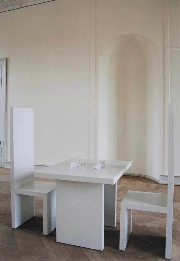 two white wooden chairs, a white wooden table, and white chess pieces