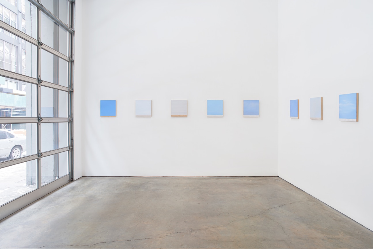 installation view of several square canvases in a sow spanning two walls