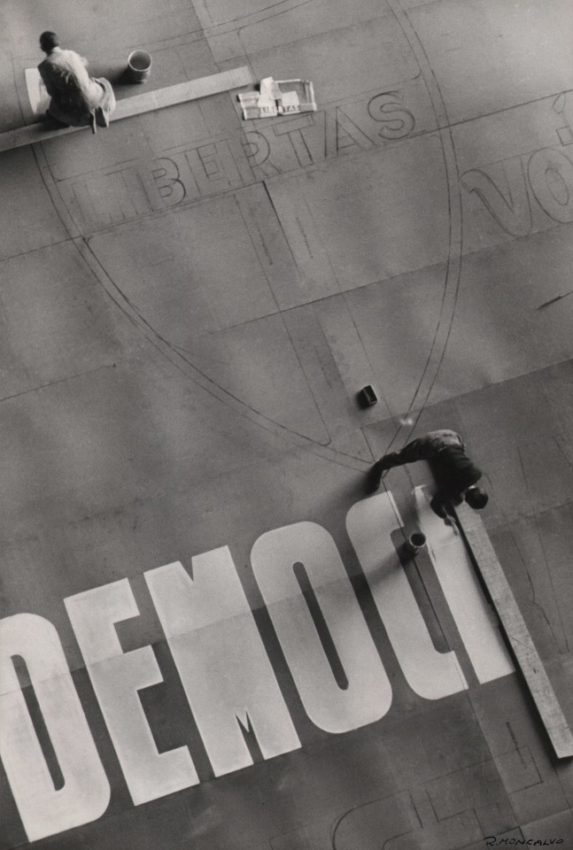 Riccardo Moncalvo, Campagna Elettorale, ​1948. Two men photographed from above painting a mural on the ground featuring a crest and white lettering.