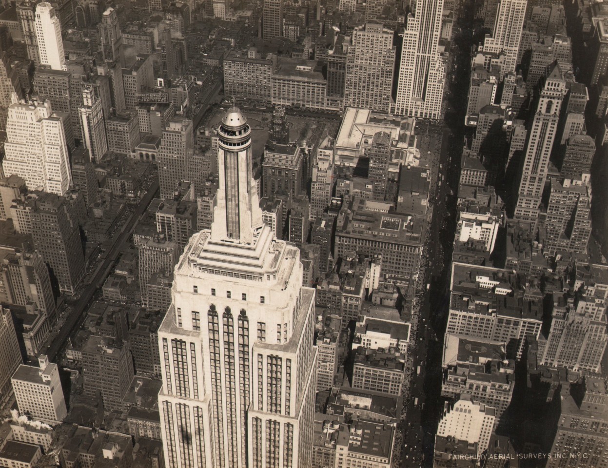 24. Fairchild Aerial Surveys, Empire State Building, Midtown, NYC, 1931. Aerial view of the top half of the Empire State Building, photographed from the above and to the right. Other city buildings and streets can be seen below.