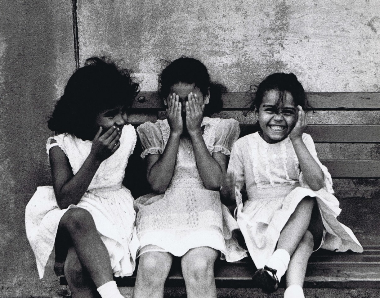 35. Beuford Smith, Three Girls, Bronx, 1968. Three girls in white dresses seated on a bench. From left to right, one has a hand to her mouth, the next has hands covering her eyes, the last has one hand covering an ear.