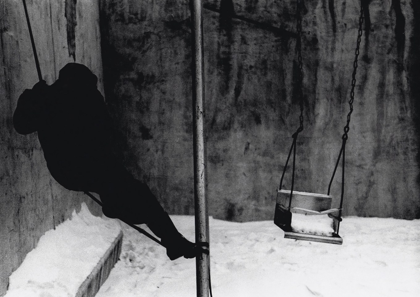 35. Beuford Smith, Boy on Swing, Lower East Side, ​1970. Silhouetted figure in black on a swingset. The ground is covered in snow.