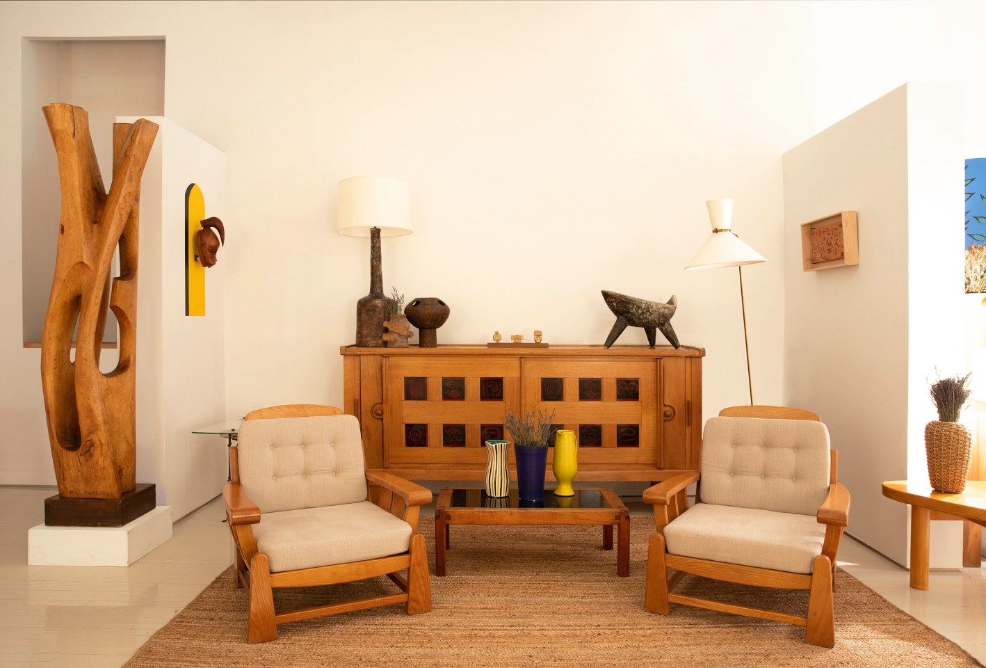 Installation view of exhibition. Pieces from left to right are Paul de Ghellinck's large sculpture, Ren&eacute; Buthaud's ceramic mask, Maison Regain's pair of armchairs, Guillerme et Chamrbon's sideboard with R. Vigeant's ceramic lamp, Alain Girel's ceramic vase, French 1960/70s table lamp, Algae Liberaki's &quot;Trilogy&quot; sculpture, Les 2 Potiers large bowl, Pierre Chapo's &quot;T18&quot; coffee table, Robert Picault ceramic pitcher, Suzanne Ramie's vase, Pol Chambost's pitcher, Robert Mathieu's floor lamp, Andr&eacute; Bizette's wall sculpture, and Audoux-Minet's vase on top of Charlotte Perriand's side table