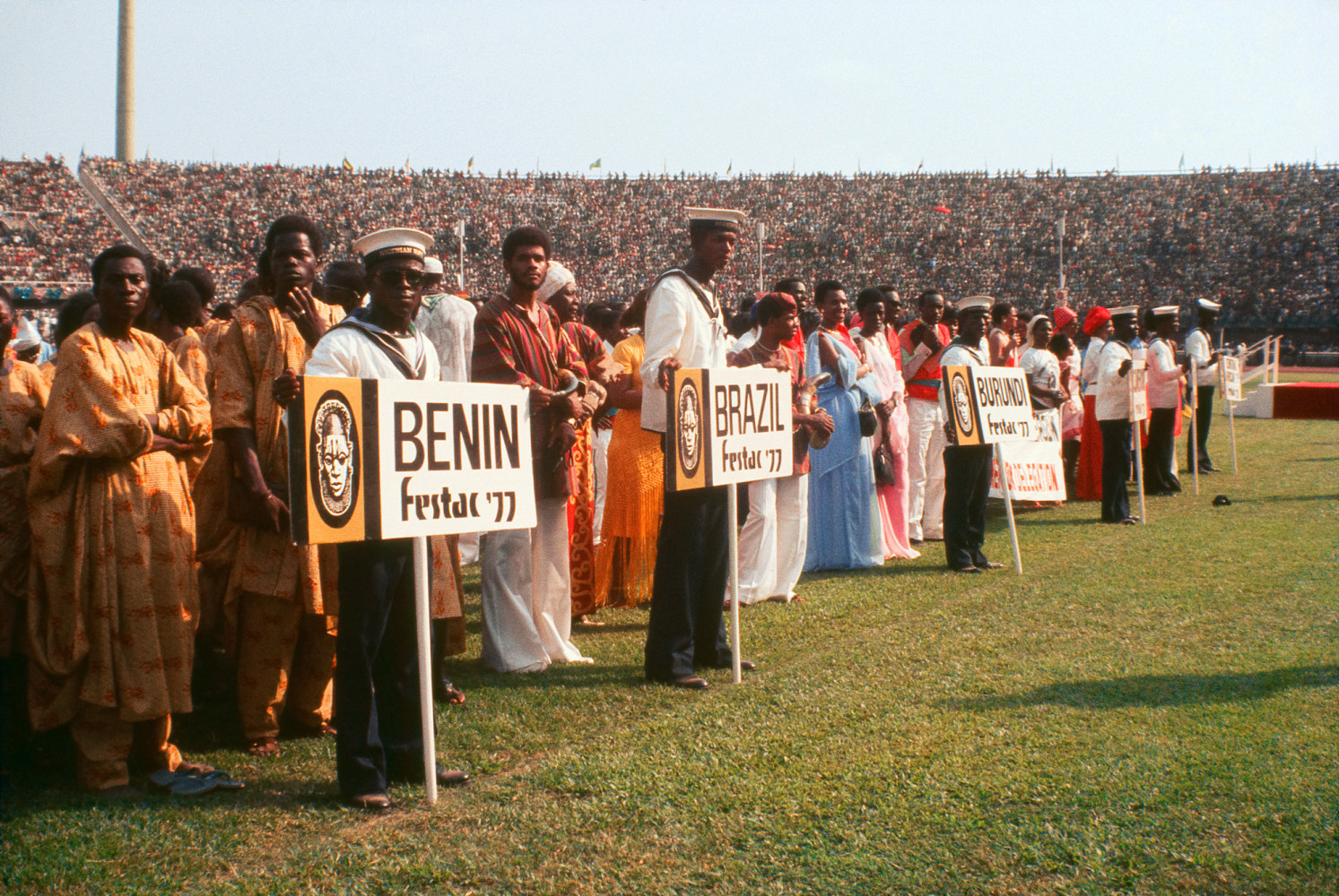 Roy Lewis (b. 1937)
FESTAC Participants Line Up Behind Their Country Name in Stadium on Open Day, 1977
Archival inkjet print on Simply Elegant Gold Fibre paper
Image: 13 3/4 x 20 inches (34.9 x 50.8 cm) Sheet: 17 x 22 inches (43.2 x 55.9 cm)
Framed: 18 5/8 &amp;times; 25 3/8 &amp;times; 1 1/2 inches (47.3 &amp;times; 64.5 &amp;times; 3.8 cm)
Edition of 5, printed 2023