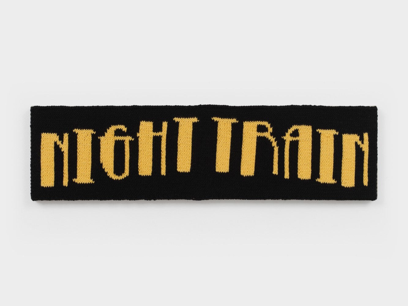 A knit artwork depicting the words &quot;Night Train&quot; in yellow yarn against a black background, sewn into linen and stretched.