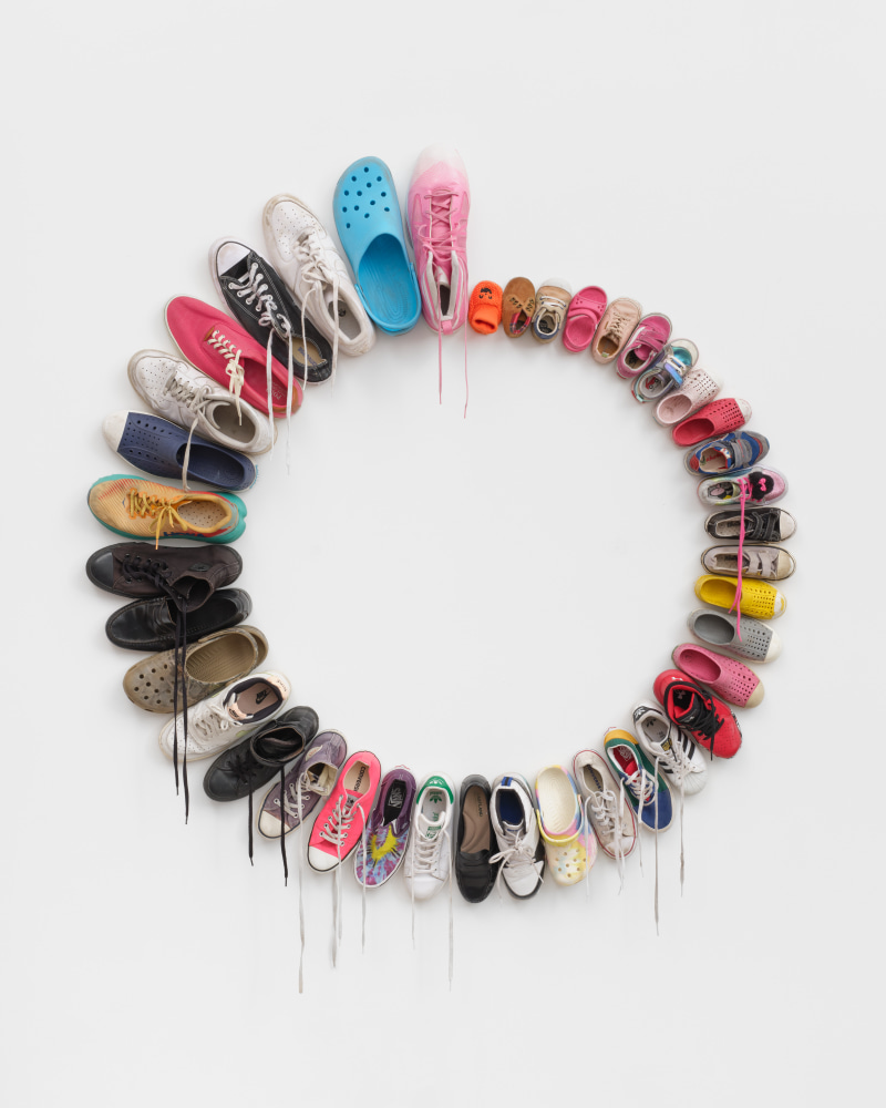 A wall mounted sculpture of shoes in a circle starting with a baby's slipper and increasing in size around the circle.