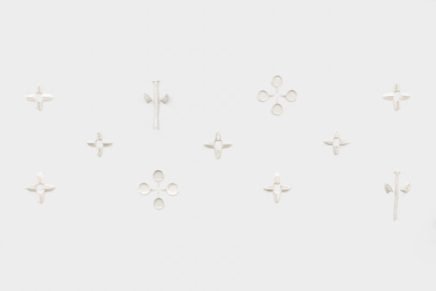 A multi piece wall mounted sculpture with ceramic replicas of irons, cast iron pans and rakes hung in groups of three and four along the wall making a star like pattern.