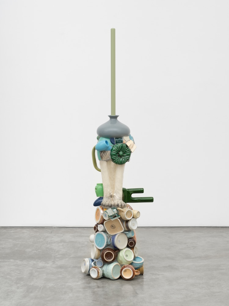 A free standing composite ceramic sculpture made from mugs, various vessels, the feet of a feline figurine and a plunger.