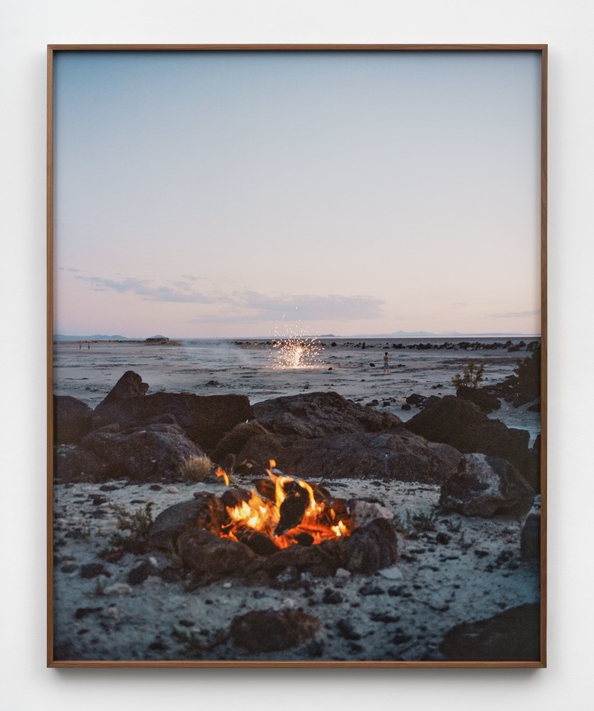 A photograph of a campfire near &quot;Spiral Jetty&quot; with fireworks going off in the background.