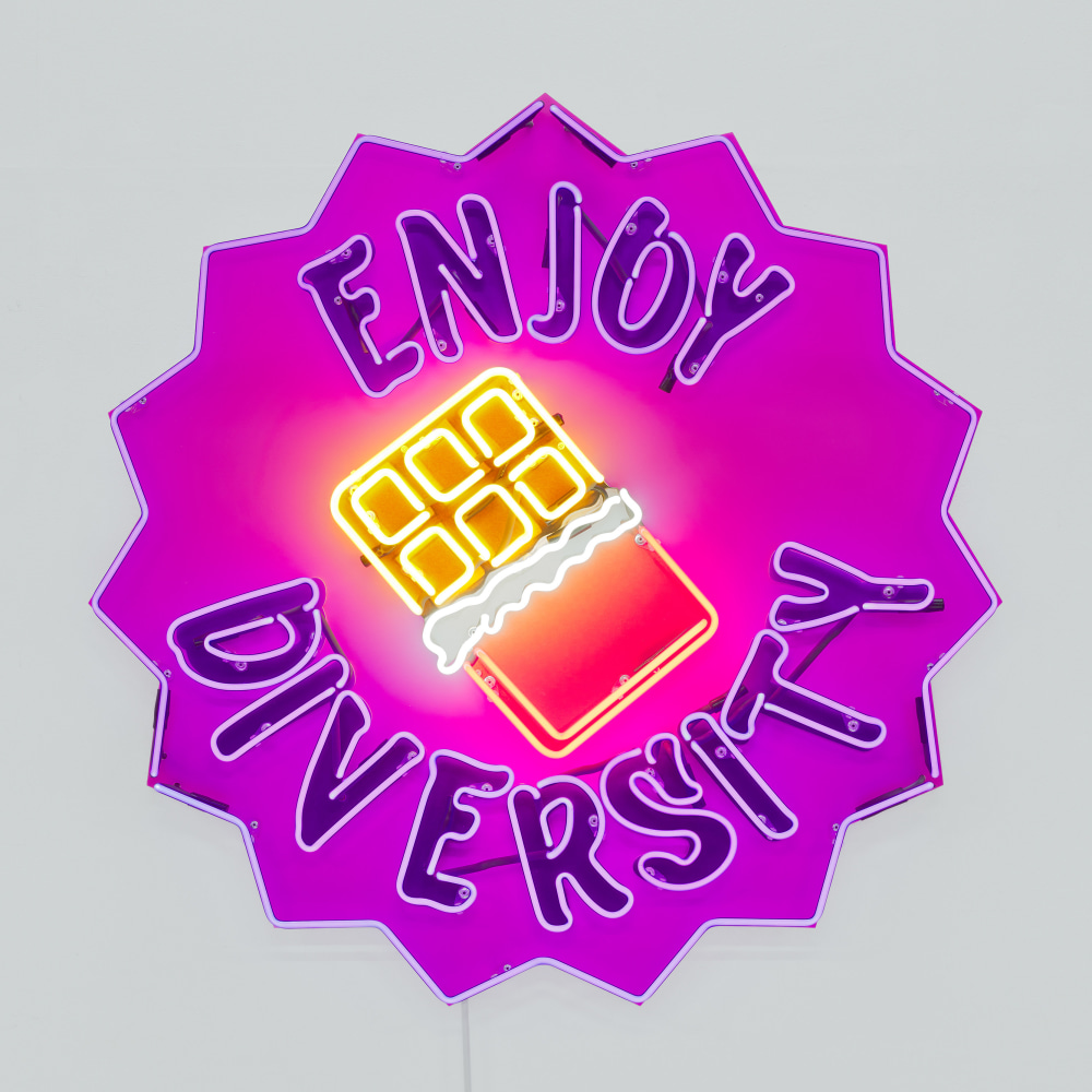 A wall mounted neon sculpture with the words &quot;Enjoy Diversity&quot; around a partially opened chocolate bar.
