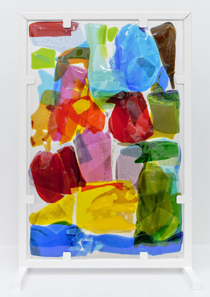 A free standing sculpture of stained glass with blocky swatches of yellow, blue, red and green mounted in a white metal frame.