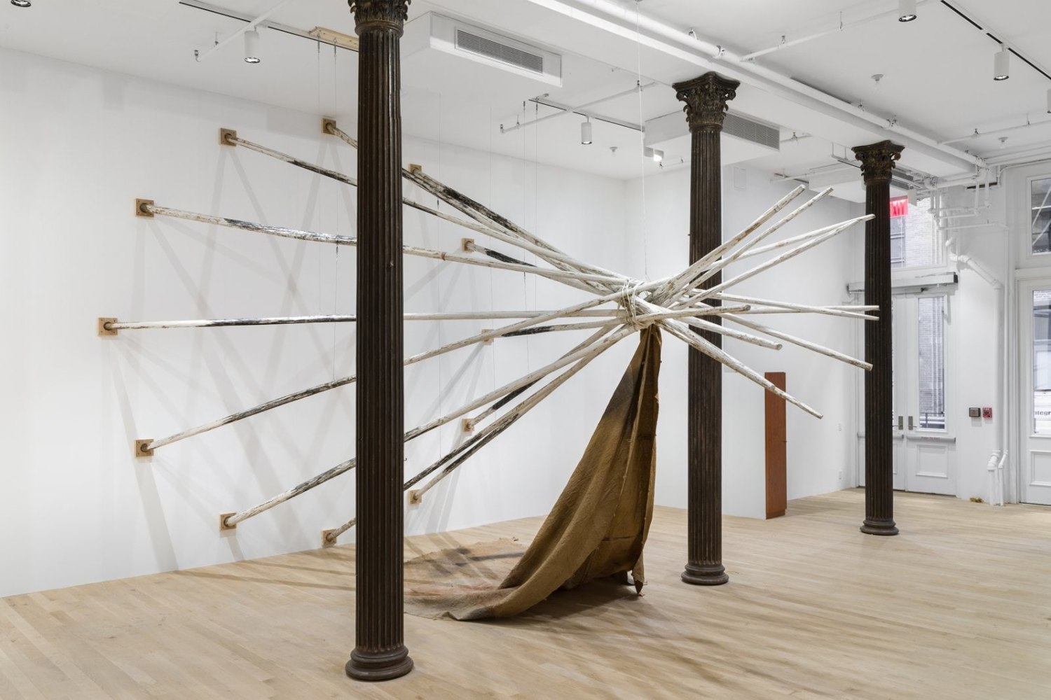 duane linklater. dislodgevanishskinground, 2019. 12 tipi poles, steel cable, white paint, charcoal, rope, digital print on linen, black tea, blueberry extract, sumac, charcoal