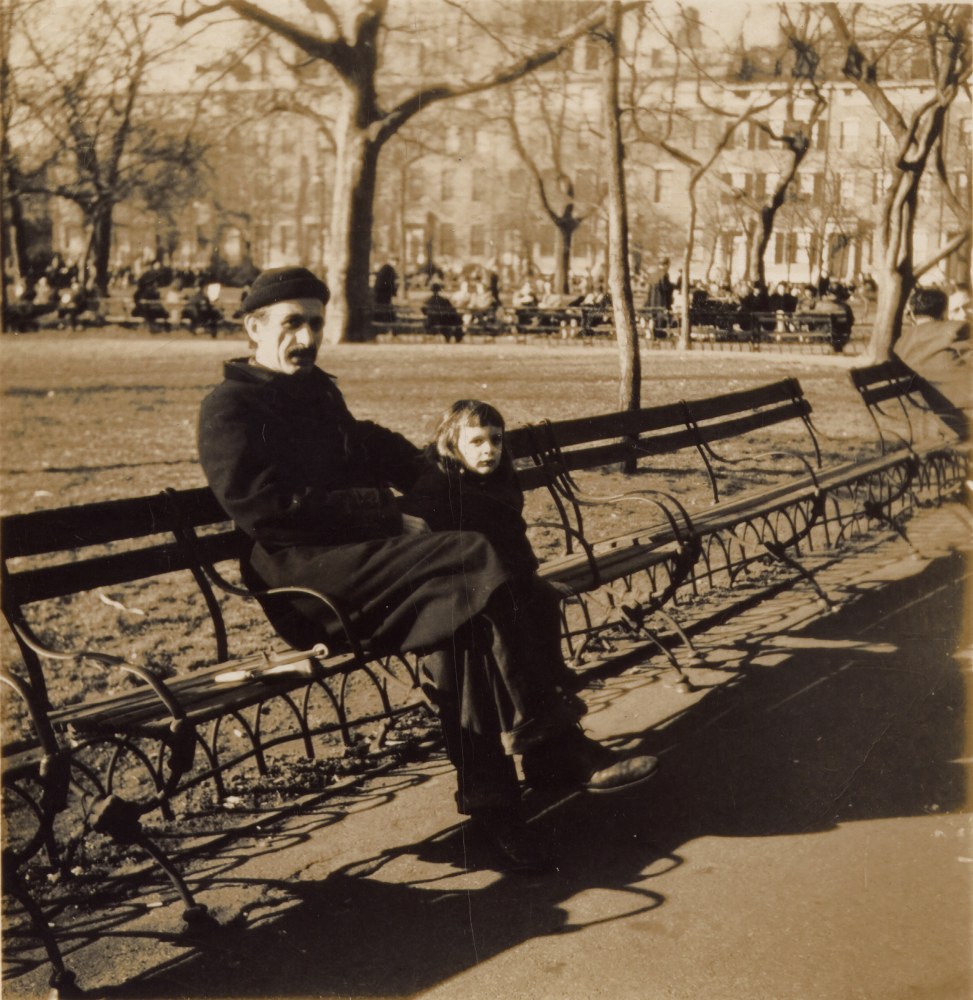 Man in a wool coat and knitted cap sitting on a park bench in New York City next to his young daughter