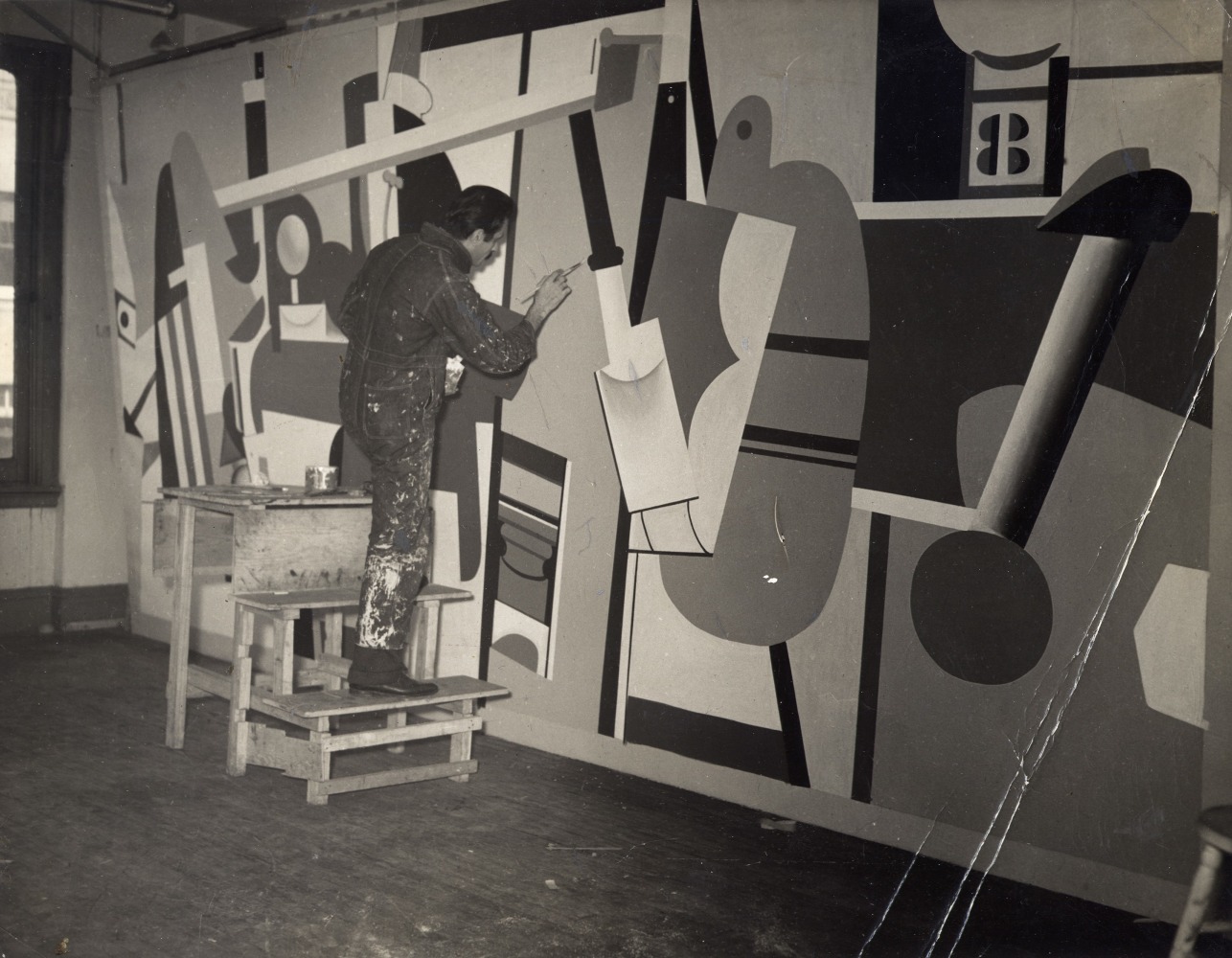 Man in dirty overalls on a step ladder painting a large abstract canvas panel suspended in a room
