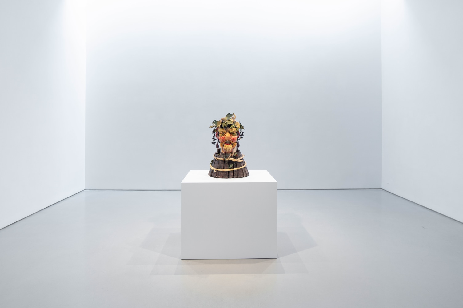 a bust of fruits and vegetables sits on a white pedestal in a big gallery room