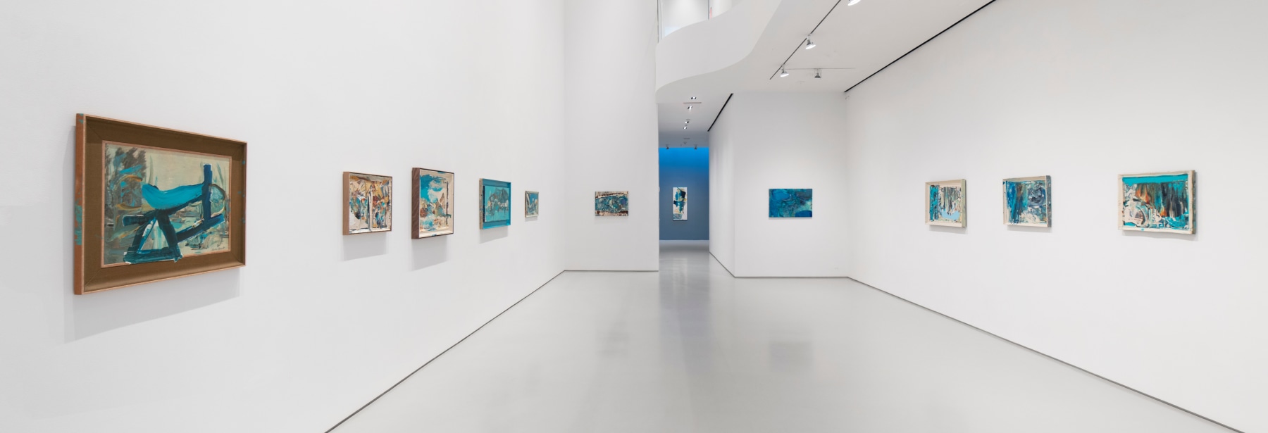 A long view of the gallery featuring a grouping of abstract paintings on parallel walls, merging towards one vertical composition at the center.