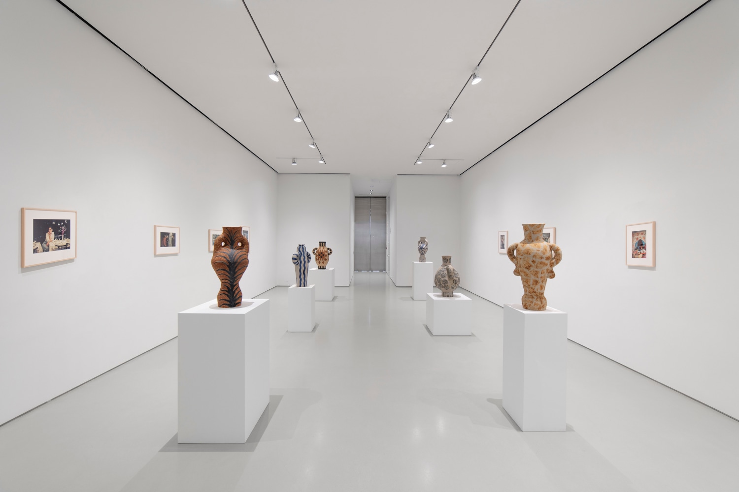 6 ceramic sculptures on pedestals in the center of the gallery and photographs hanging on two opposing white walls