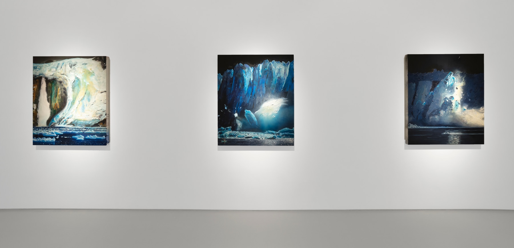 Three paintings of glaciers hang on a white wall