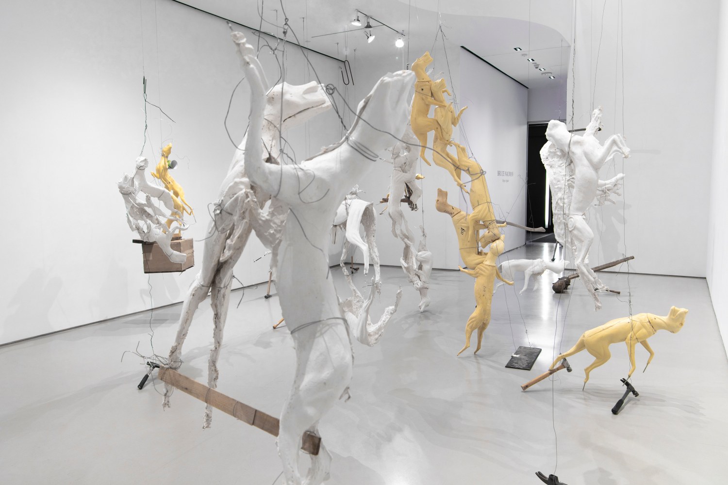 Large sculptures hanging from wire of yellow and white molds of foxes and coyotes with other industrial elements like hammers and wood