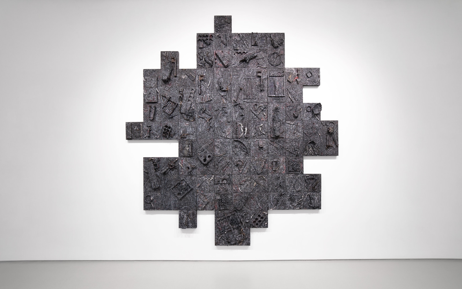 A dark, large scale, geometric artwork hung on white gallery wall.