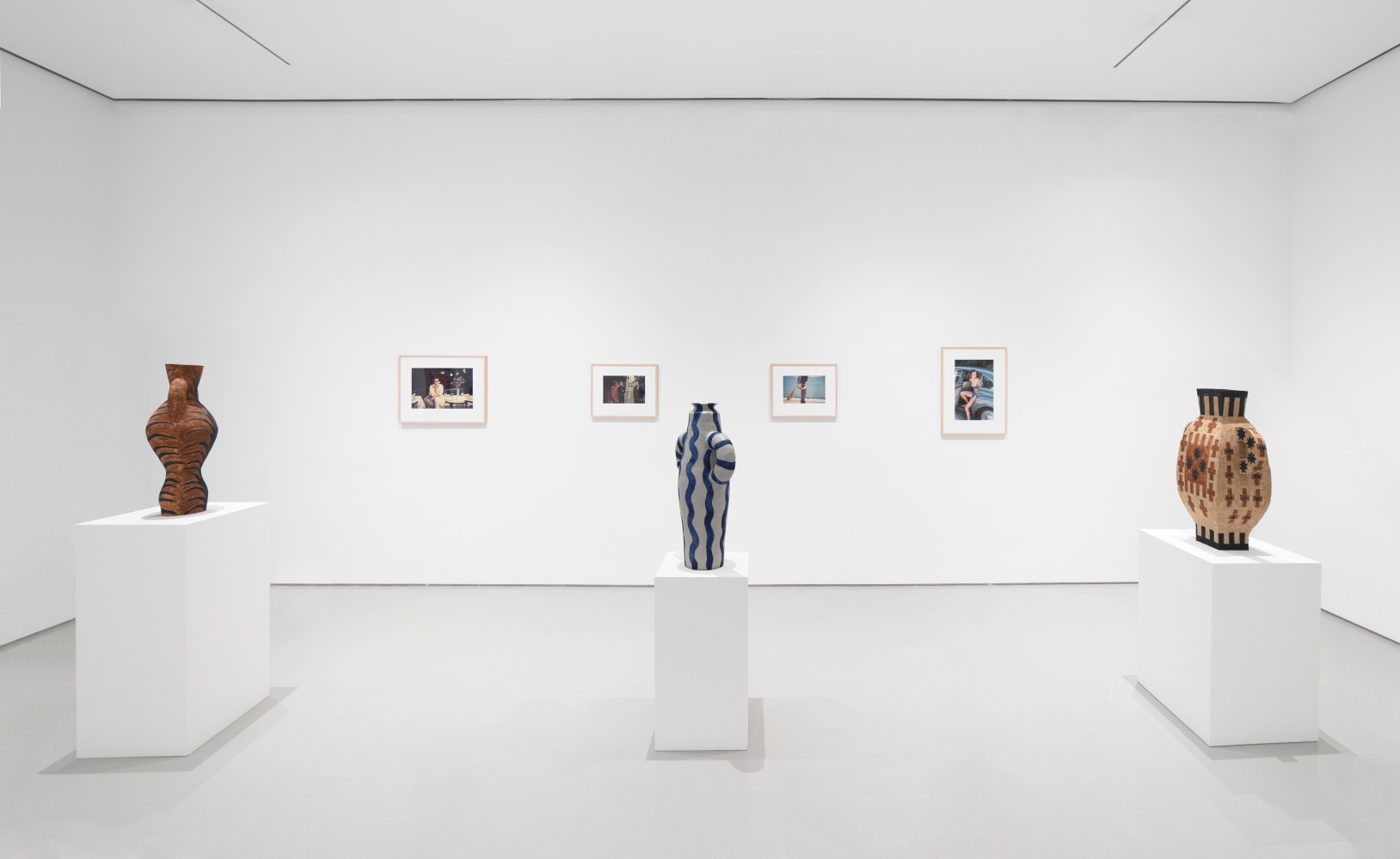 3 ceramic sculptures on pedestals with 4 photographs hanging behind on a white wall