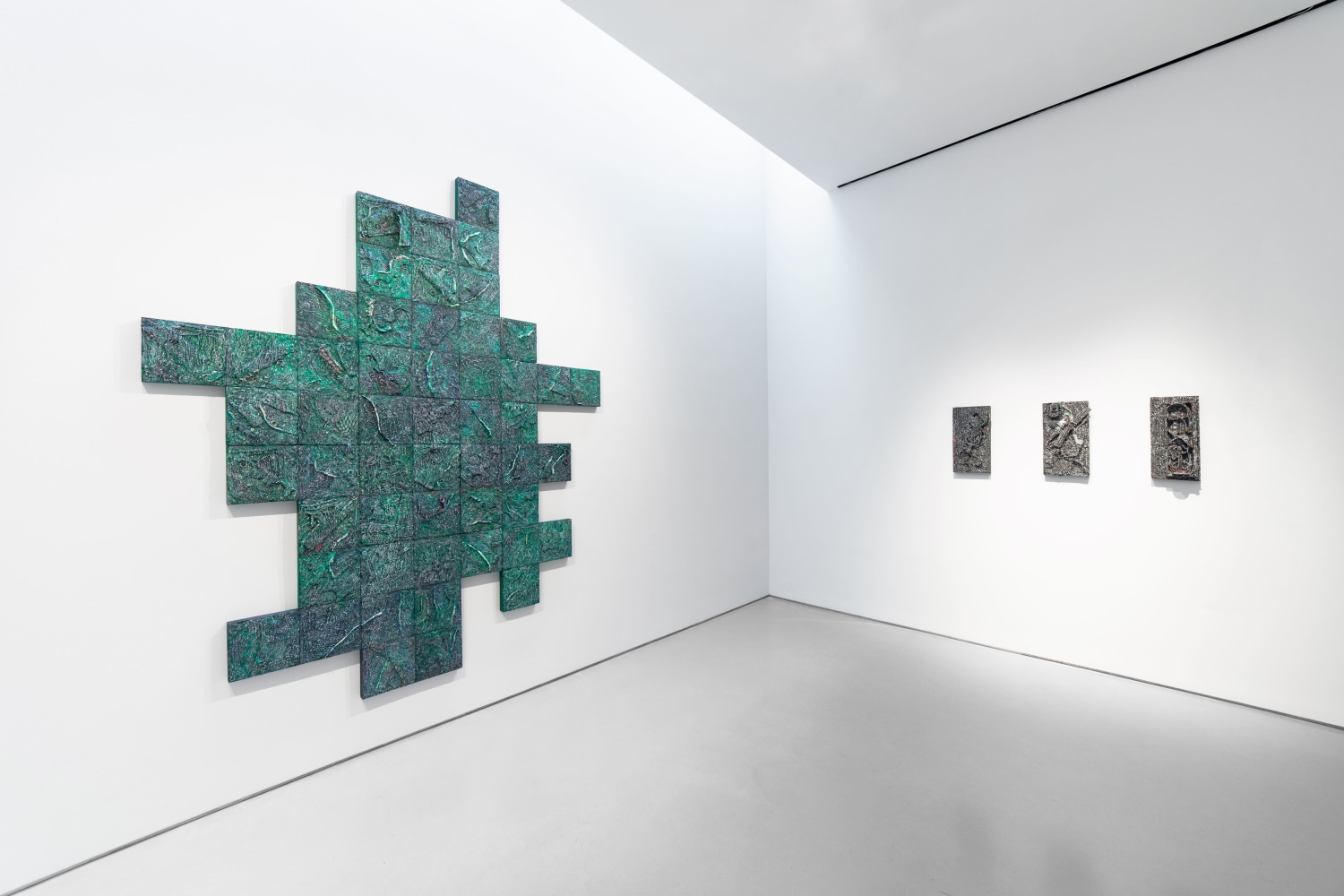 Large green geometric artwork is hung adjacent from three small dark artworks in gallery space.