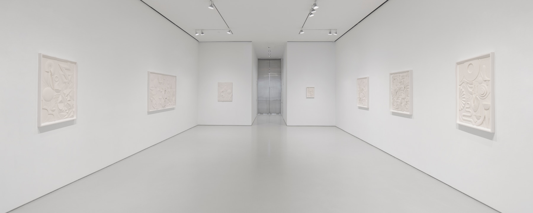 Installation view of white artworks on a white wall