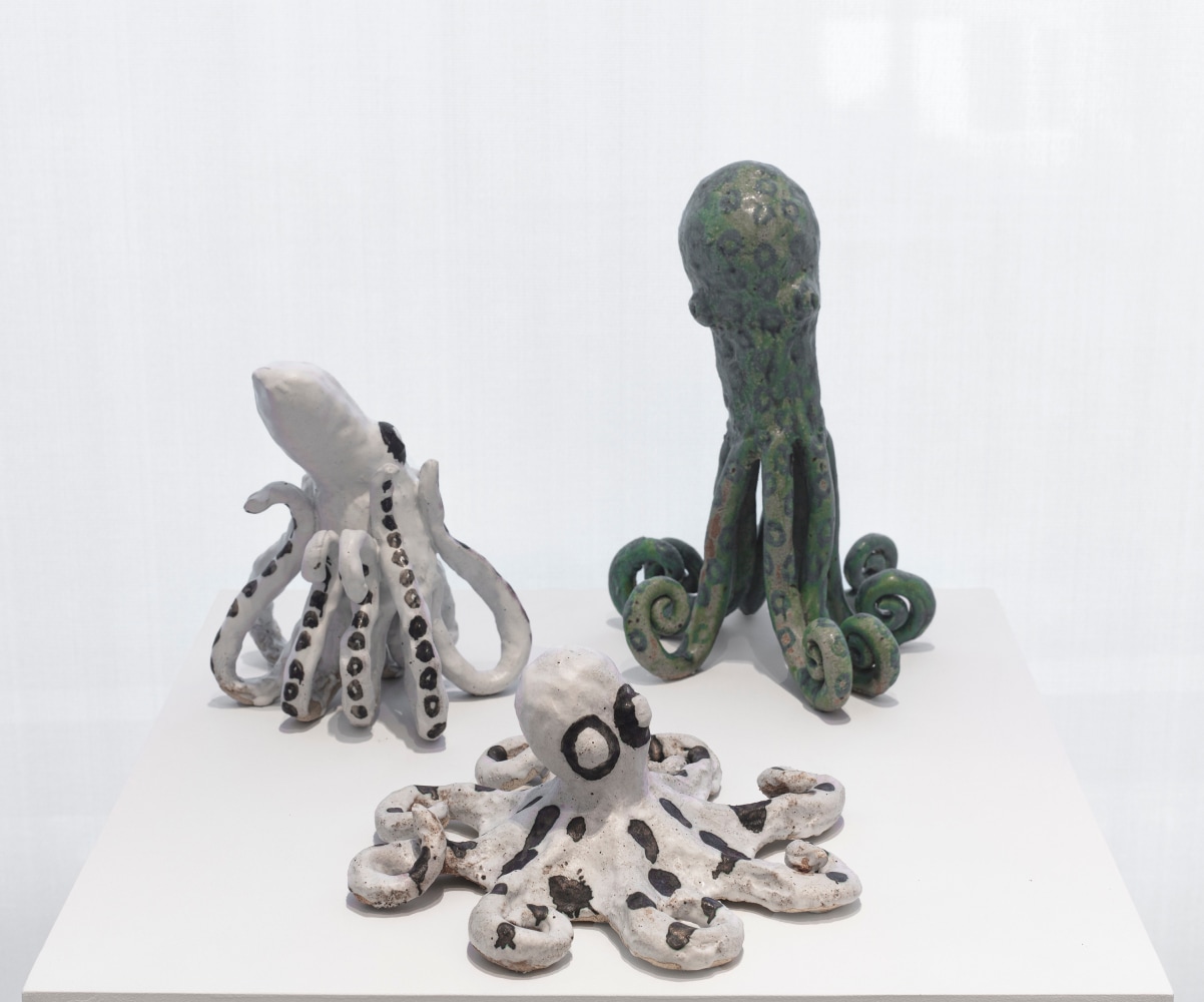 3 small ceramic sculptures of octopi displayed on white pedestal